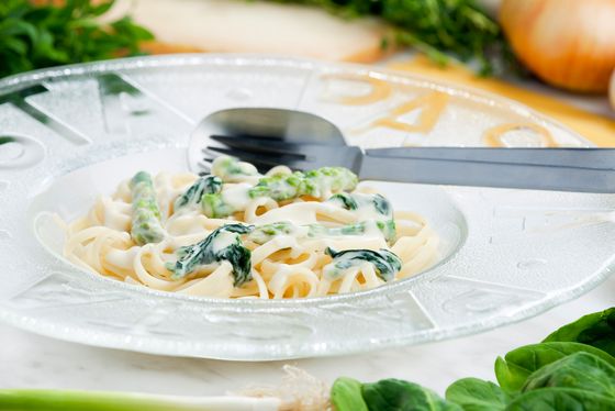 Linguini mit grünem Spargel, Ruccola & gerösteten Pinienkernen an Safransauce auf einem weißen Teller